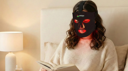 Woman reading in bed using the Fresh Healthcare LED Face Mask to help improve the appearance of skin texture and tone
